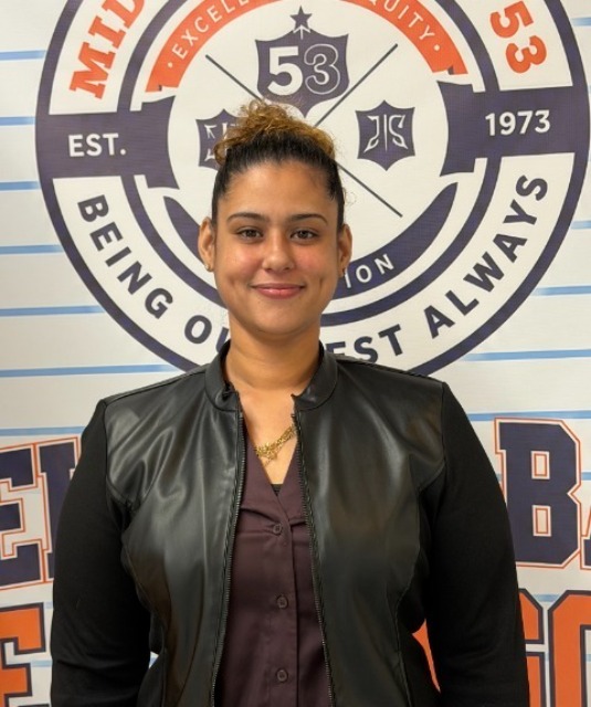 Ms. A. Rivera smiling in front of MS 53 school banner