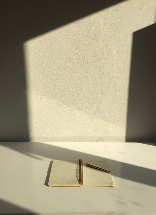 An open spiral notebook and pen on a sunlit desk.