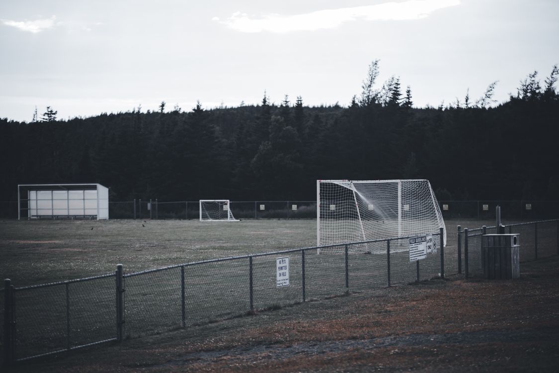 An empty soccer field with goalposts, fencing and trees.