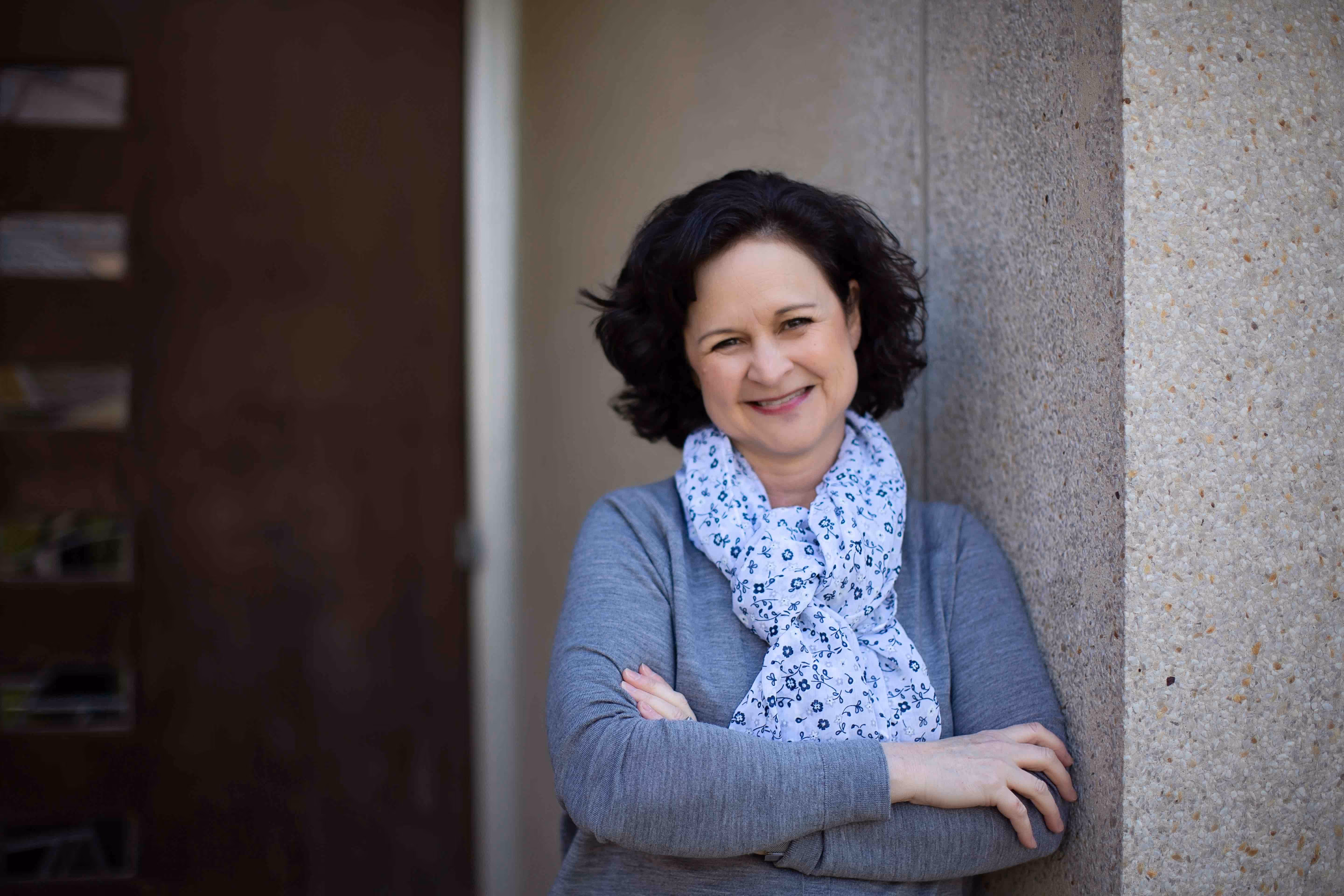 portrait of stephanie stollar leading against a cement wall in front of a door