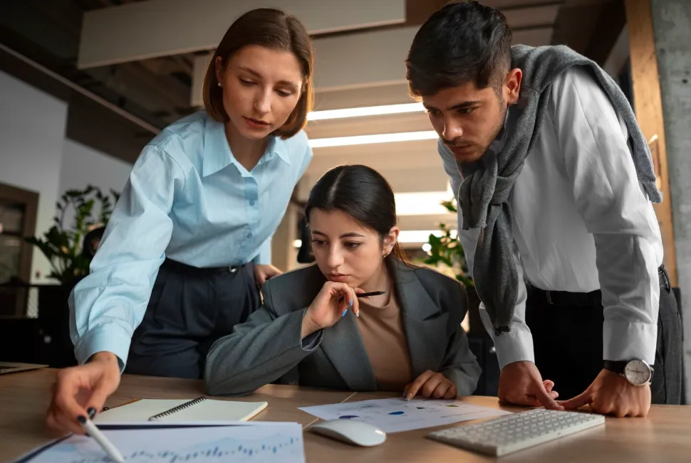 Tres jóvenes profesionales revisan documentos con gráficos en una oficina moderna.