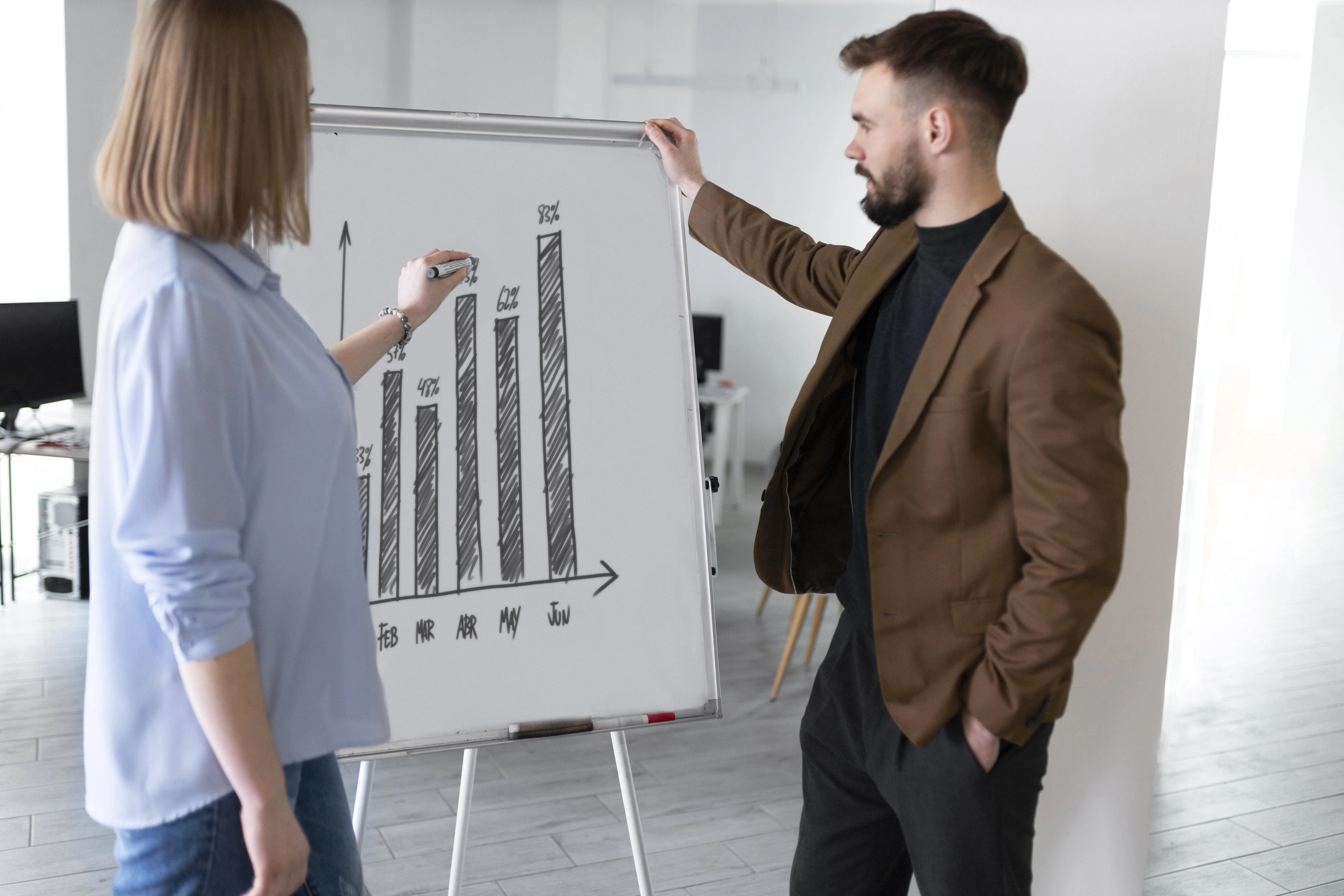 Dos personas discutiendo un gráfico de barras dibujado en una pizarra blanca en una oficina.