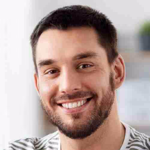 Hombre joven con barba y cabello corto, sonriente, con camiseta de rayas blancas y negras.
