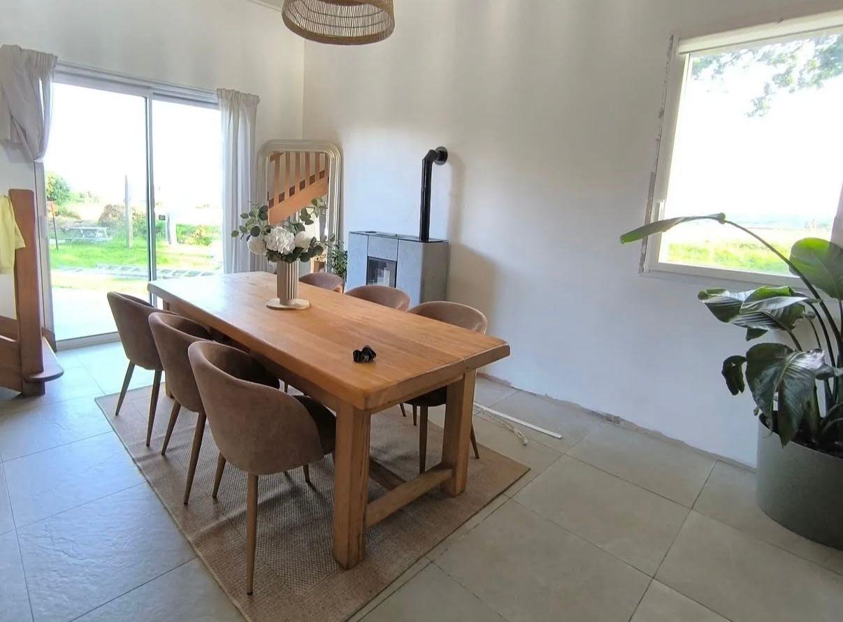 salle à manger lumineuse : murs blancs, grandes dalles, table en bois et poêle près de la baie vitrée.
