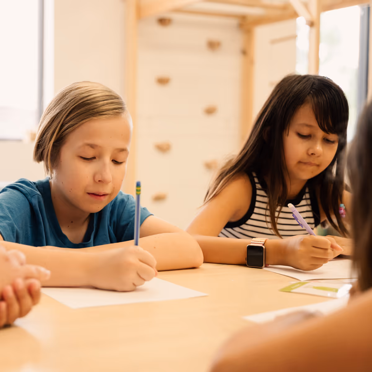 A boy and girl sitting at a table with paper and pencil.