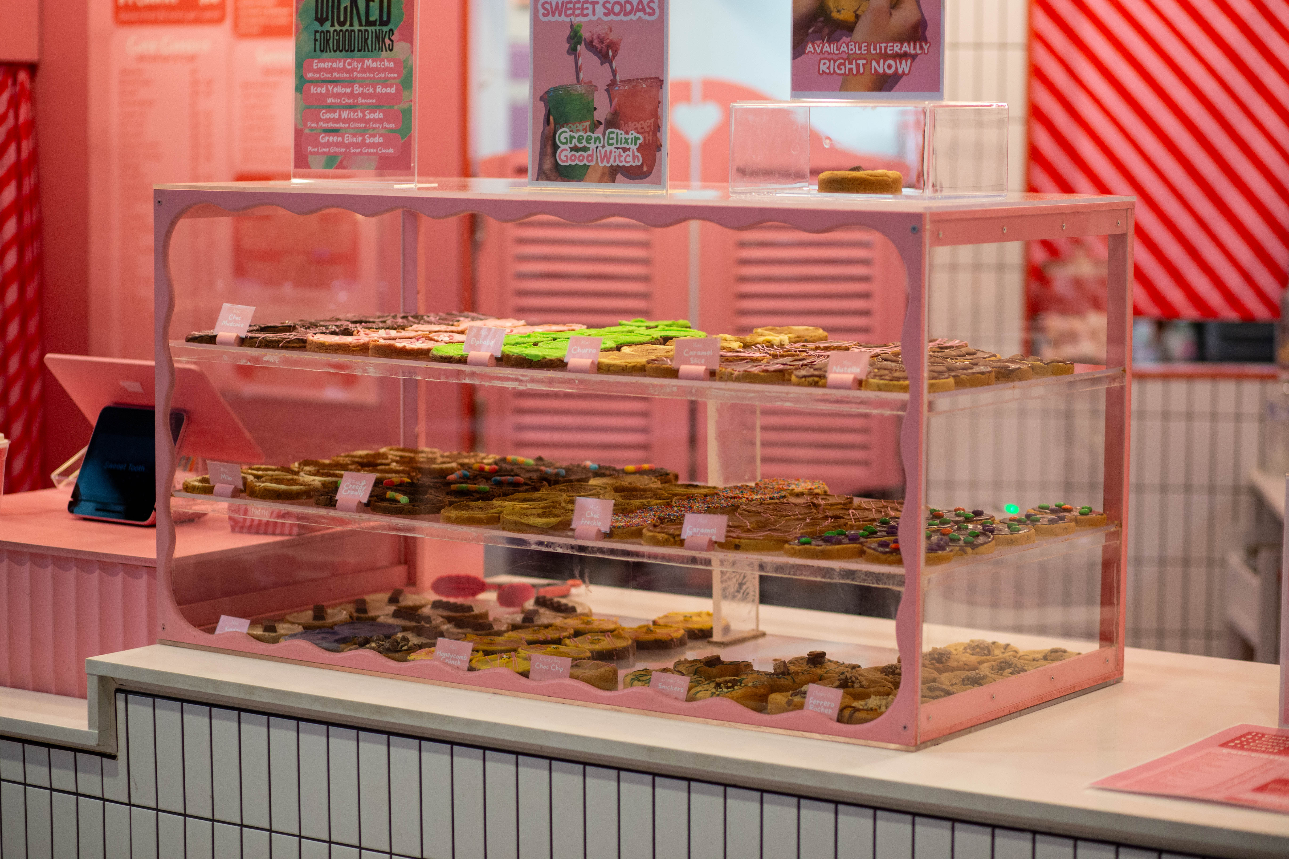 Pink display case holding multiple rows of decorated cookies in a bright pink bakery shop.