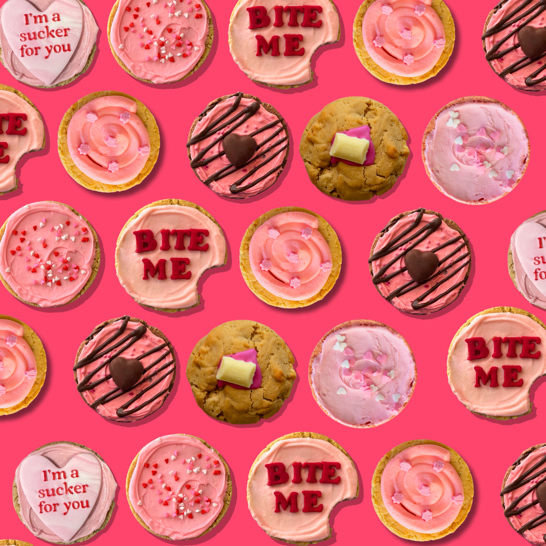Variety of colourful decorated cookies with frosting, sprinkles, chocolate, and toppings on a pink background.