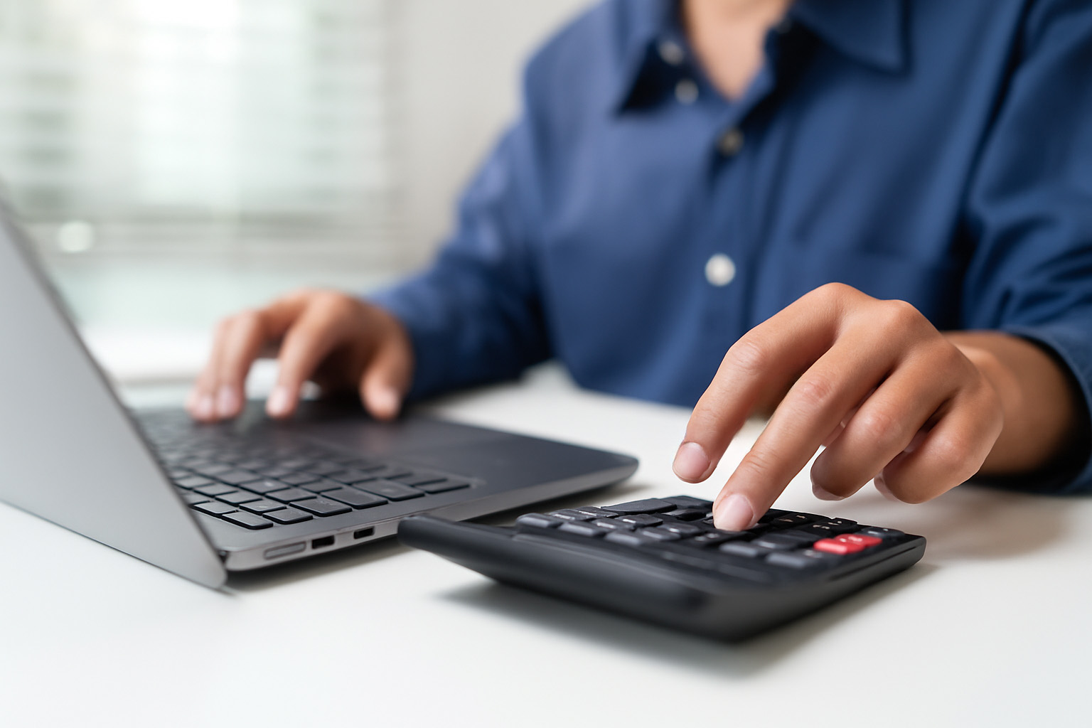 Business professional working on laptop and calculator, managing finances at a desk.