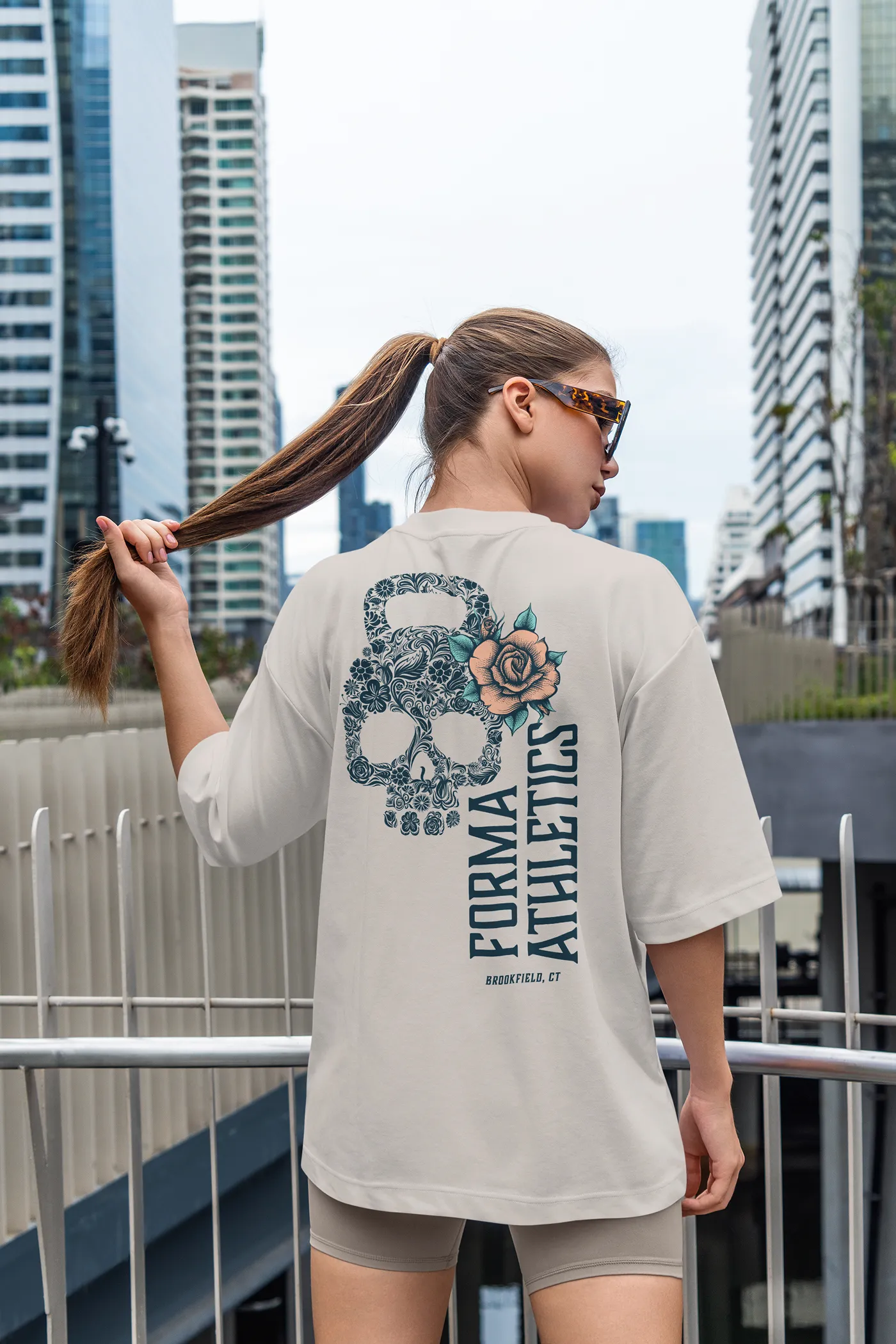 A woman showing a design on the back of a Forma Athletics tee shirt.
