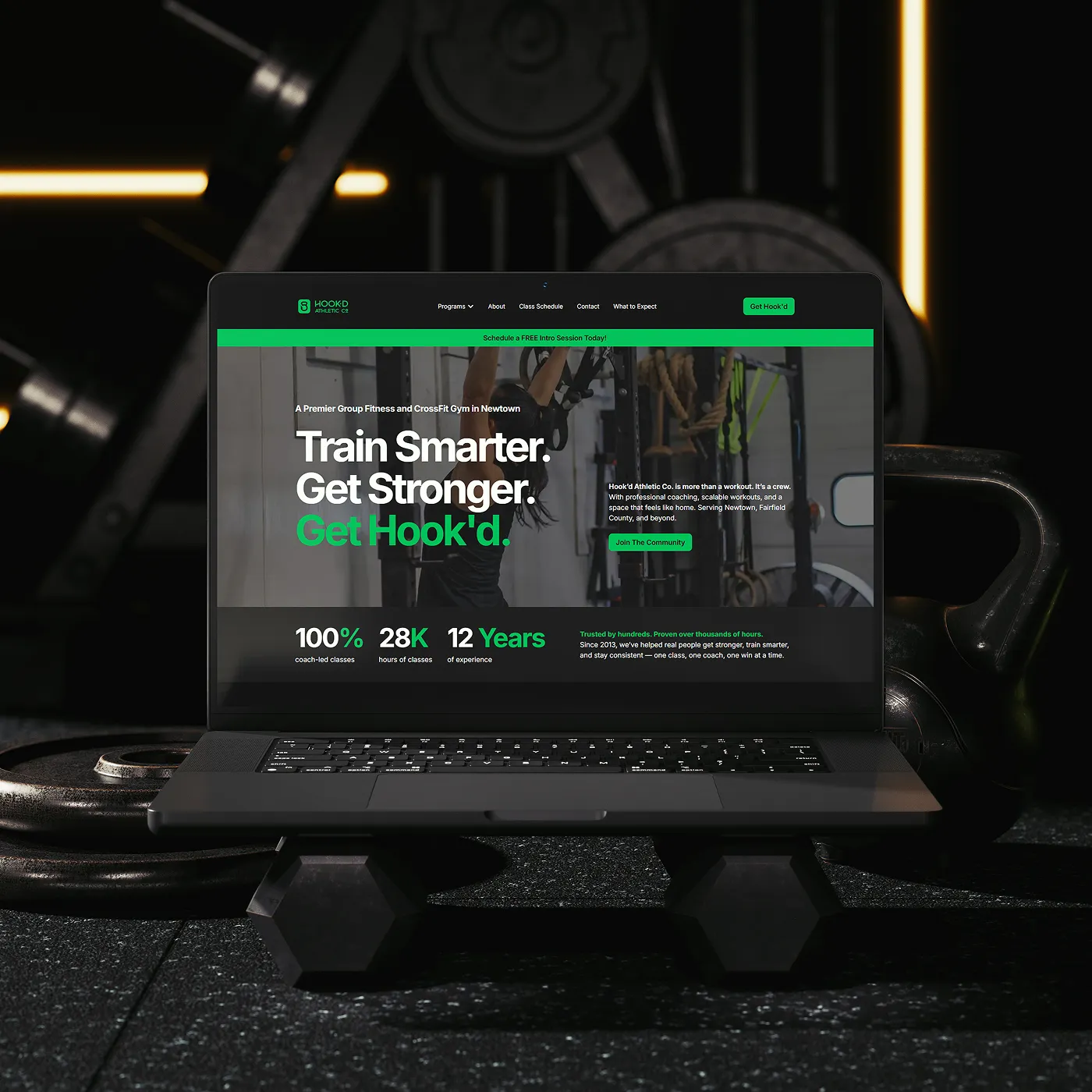 A laptop showcasing the Hook'd Athletic Co. website with gym objects in the background.