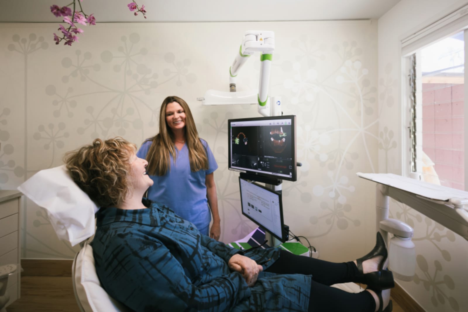 Female dentist in chair examining patient in dental operatory with equipment visible