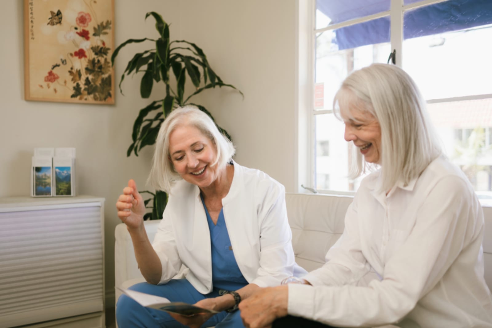 Two female dentists consulting with patient in bright dental office with plants