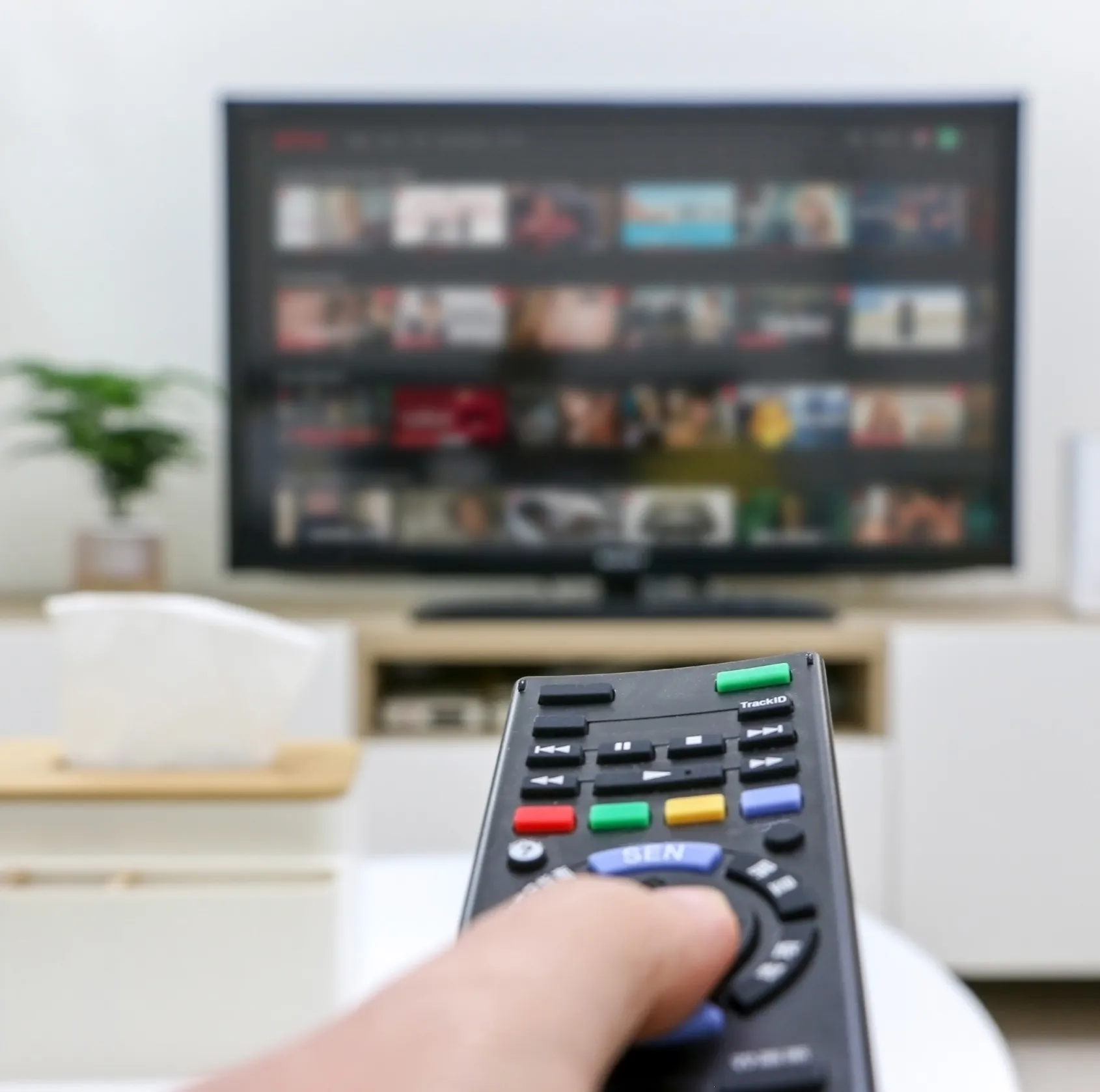A hand holding a remote control in front of a television.