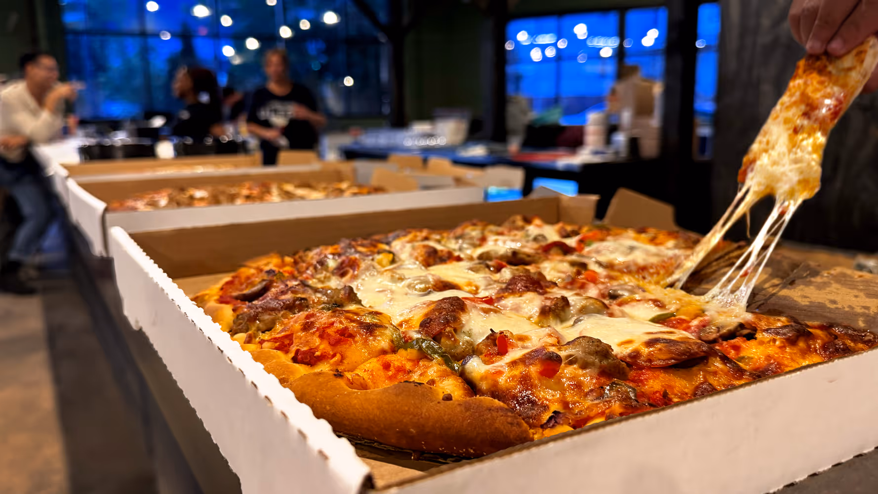 Hot, fresh pizza displayed on the bar, with one piece being taken, resulting in a cheese pull.