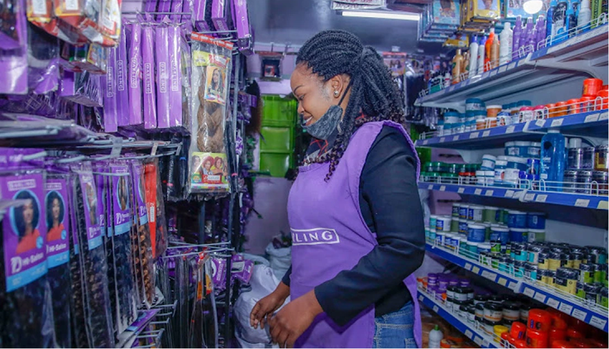 A stylist wearing a purple Darling apron looks at shelves stocked with hair extensions and beauty products inside a salon supply store.