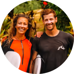 Smiling man and woman standing close together outdoors, each holding a surfboard.