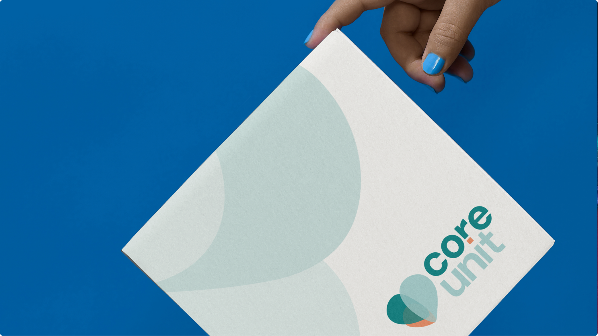 Hand with blue nail polish holding a white package with teal and orange Core Unit logo on a blue background.