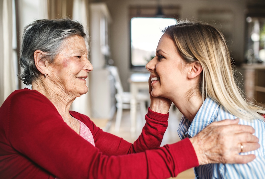 Adult daughter smiling while her aging mother caresses her face.