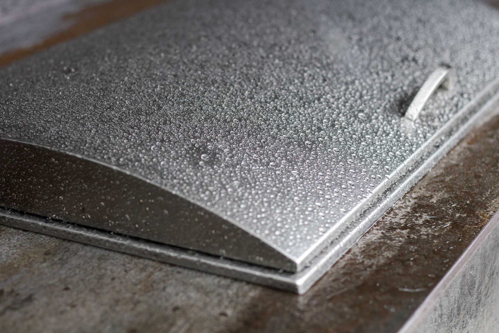 Close-up of a metallic rectangular object with a handle covered in water droplets on a textured surface.