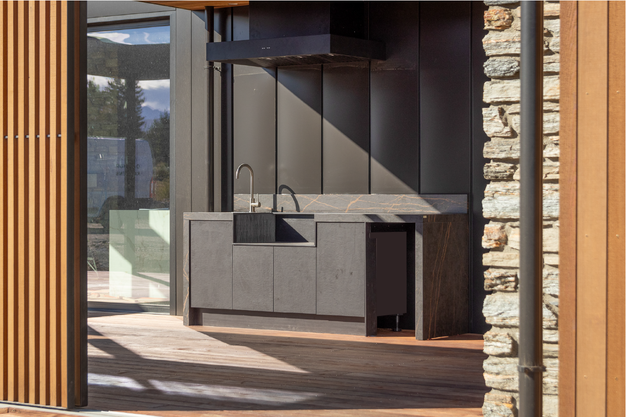 Modern outdoor kitchen with dark cabinetry, built-in sink, and wooden deck flooring.