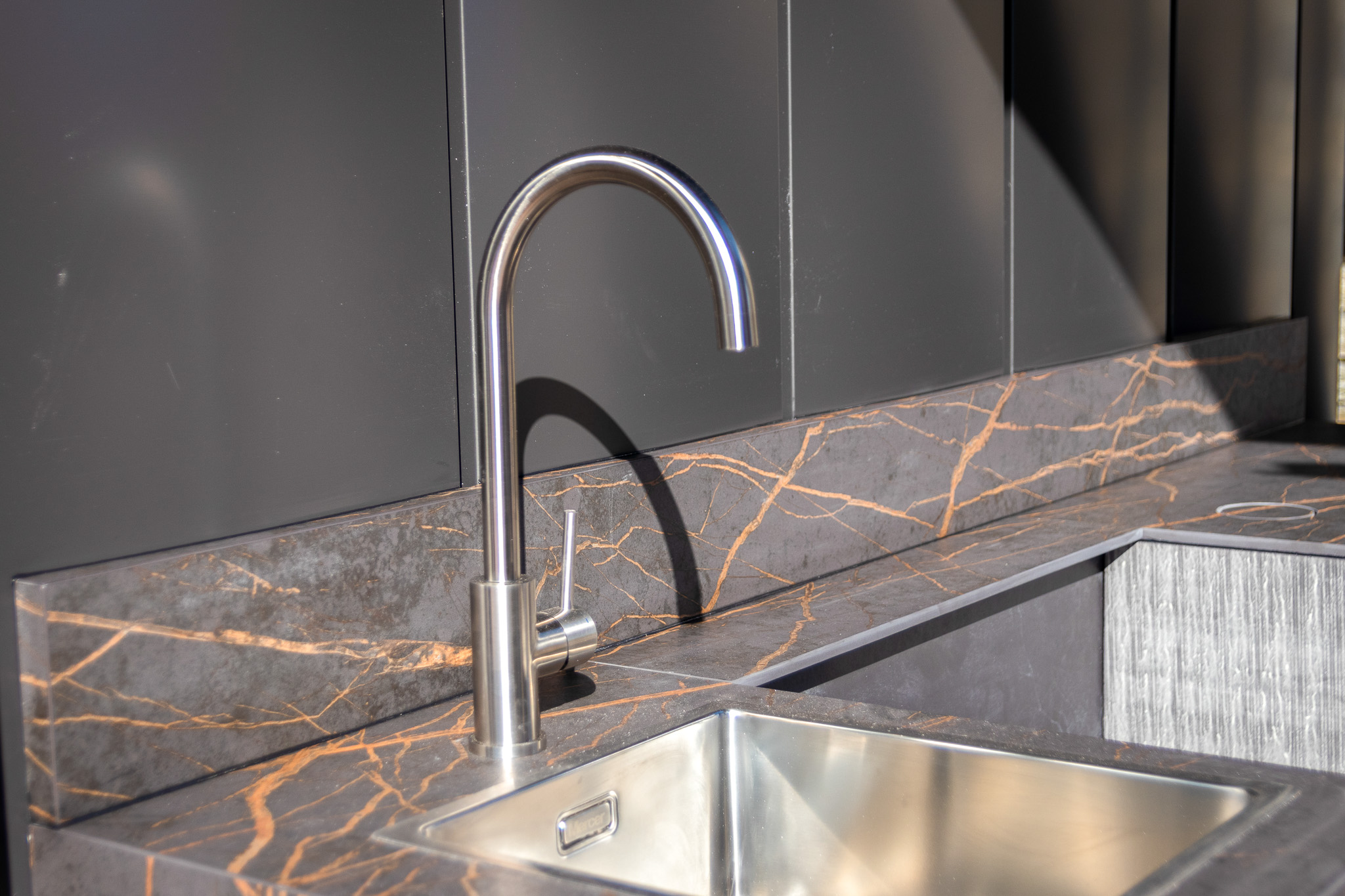 Modern kitchen sink with a stainless steel faucet and countertop featuring grey stone with orange veining.