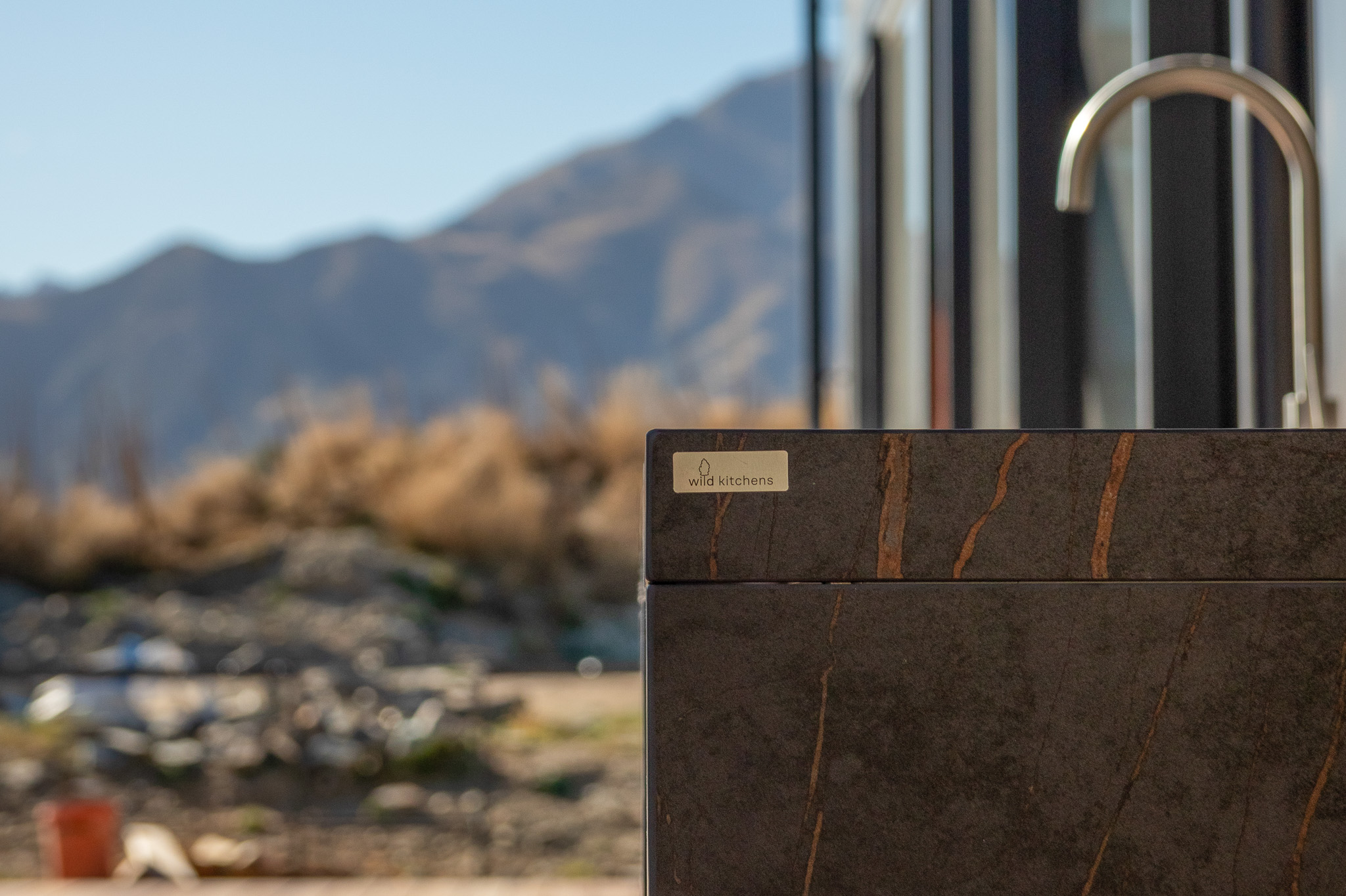 Close-up of a dark stone kitchen counter with a silver faucet and a blurred mountain landscape background.