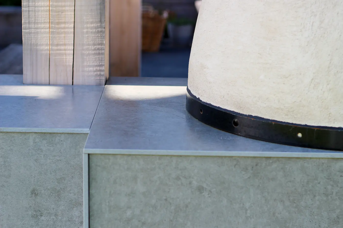 Close-up of a light stone countertop with a curved beige structure edged in black on the right and wooden posts in the background.