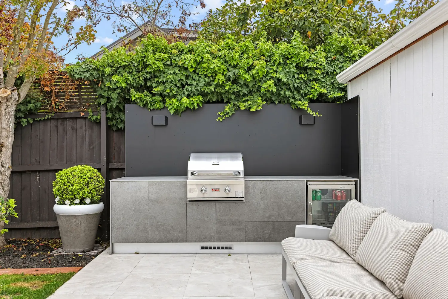 Outdoor pizza oven on a concrete countertop with stacked firewood stored below.