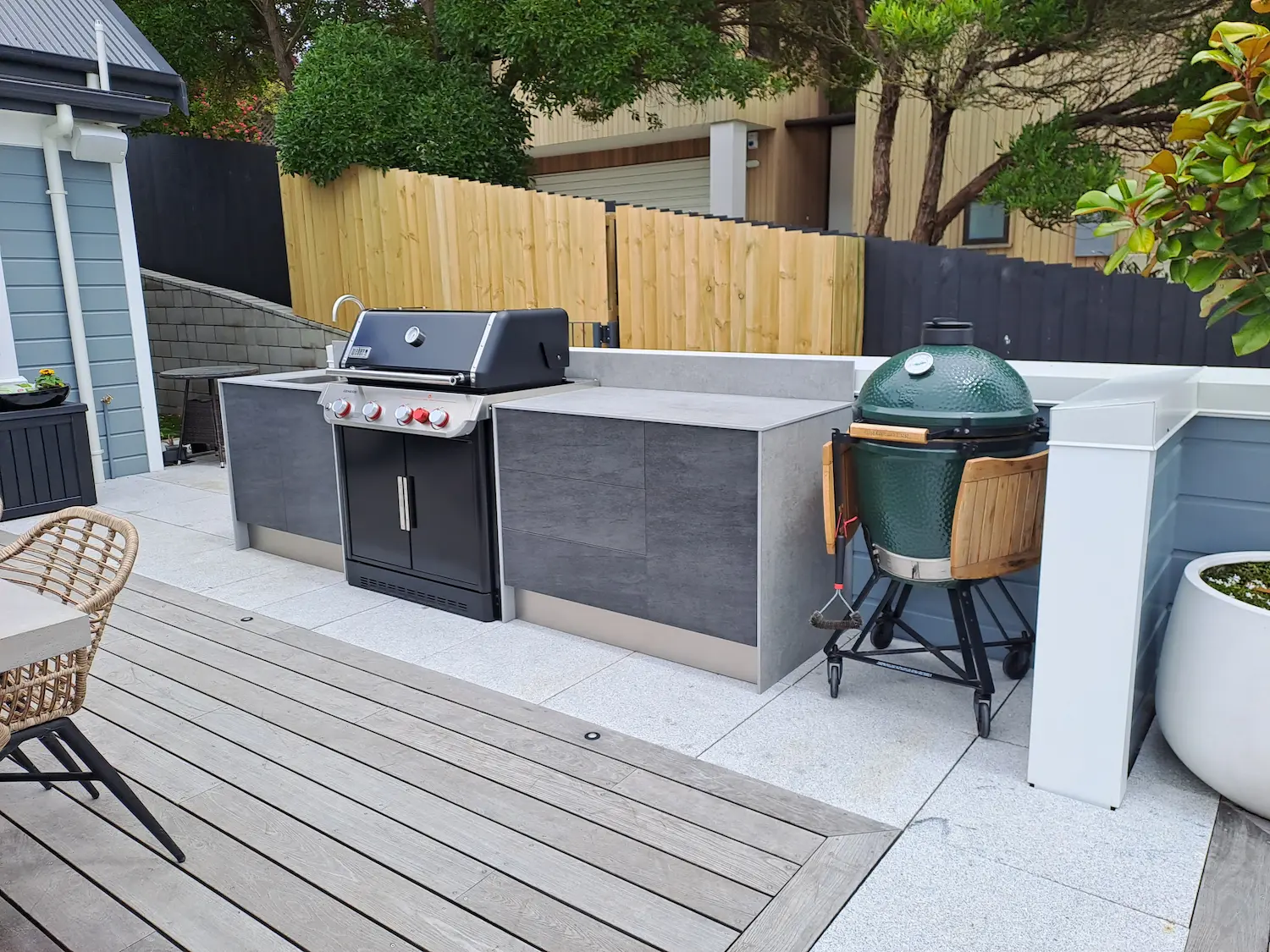 Modern outdoor kitchen setup with a stainless steel gas grill, concrete countertops, and a green ceramic egg-style charcoal grill on a patio.