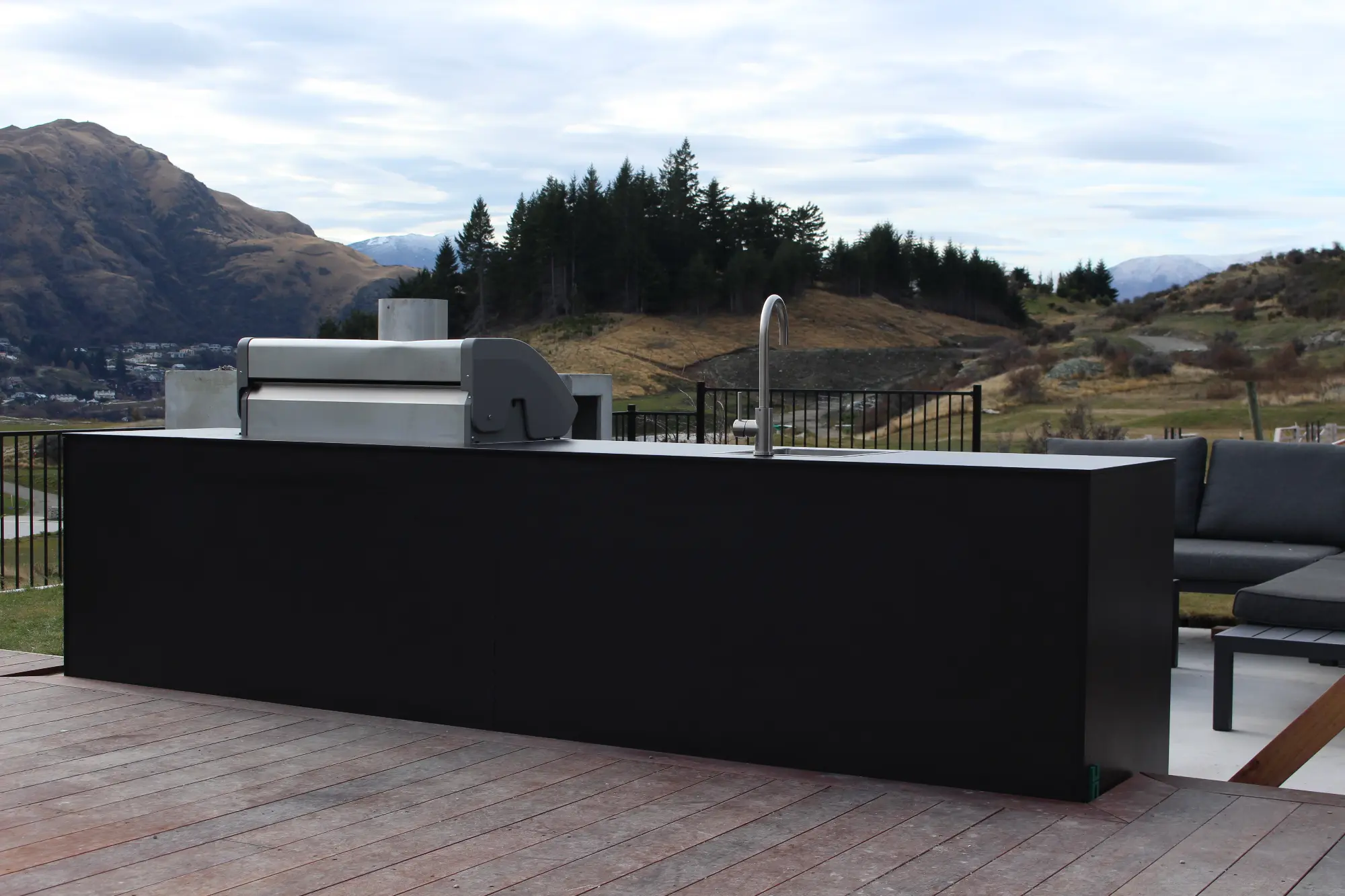 Outdoor kitchen island with a stainless steel grill and a faucet against a mountainous landscape.