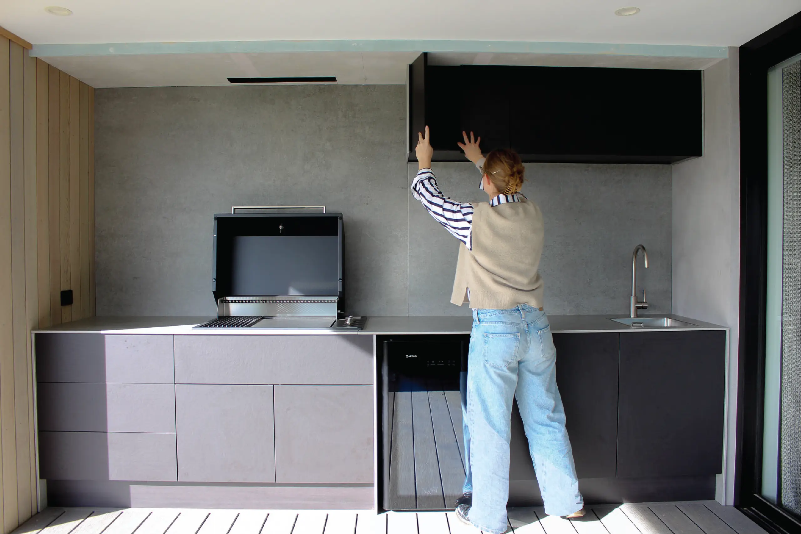A person operning the hood of a grandfire BBQ in an Outdoor kitchen