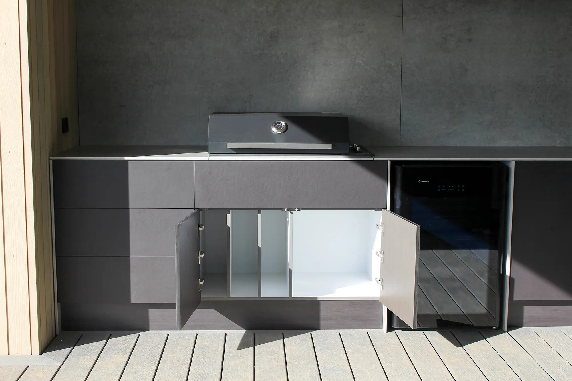 Modern outdoor kitchen unit with grey cabinets, open storage doors, a built-in grill, and a black mini fridge.
