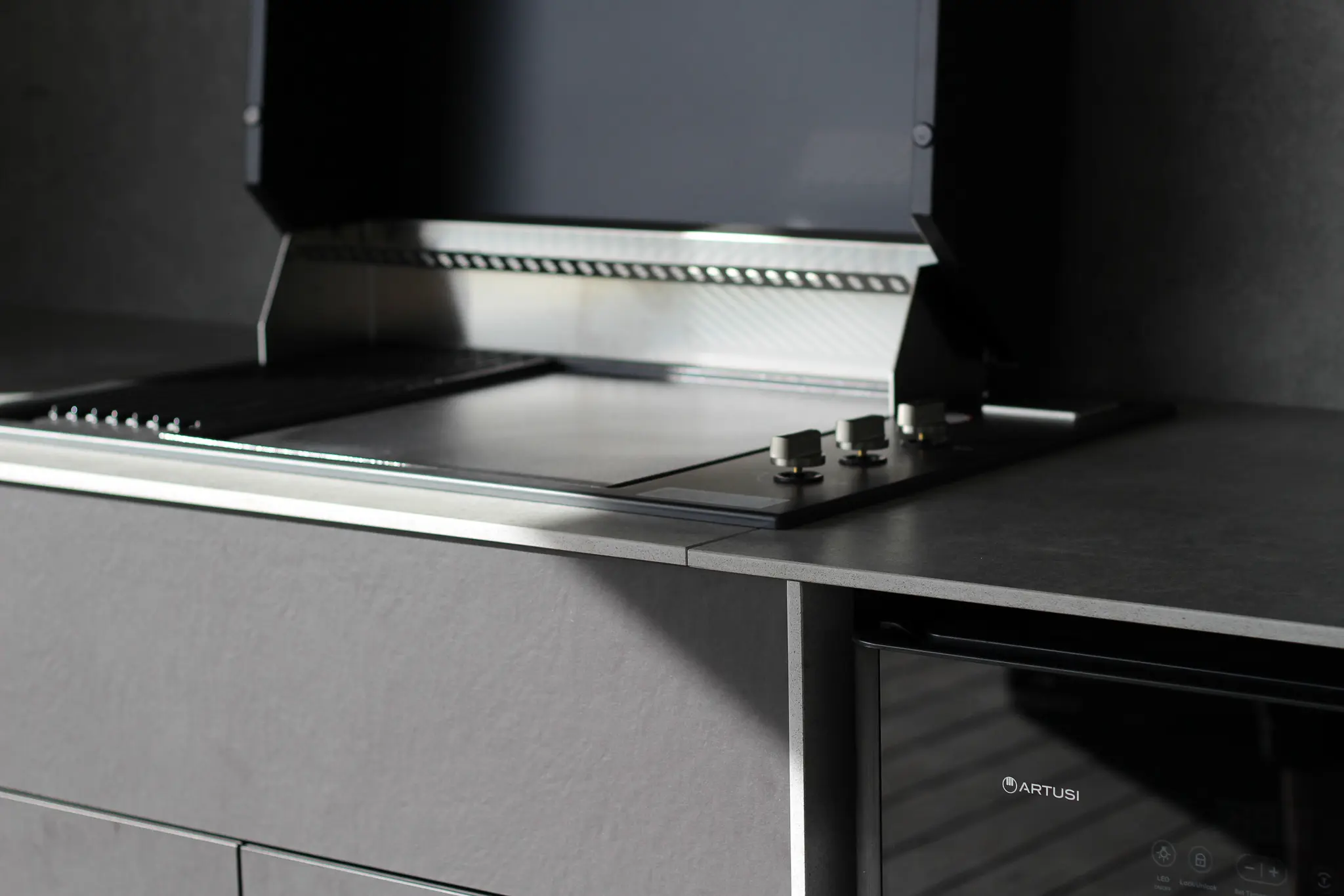 Modern Dekton stone kitchen countertop with a stainless steel grill and stove knobs, alongside a black Artusi appliance.