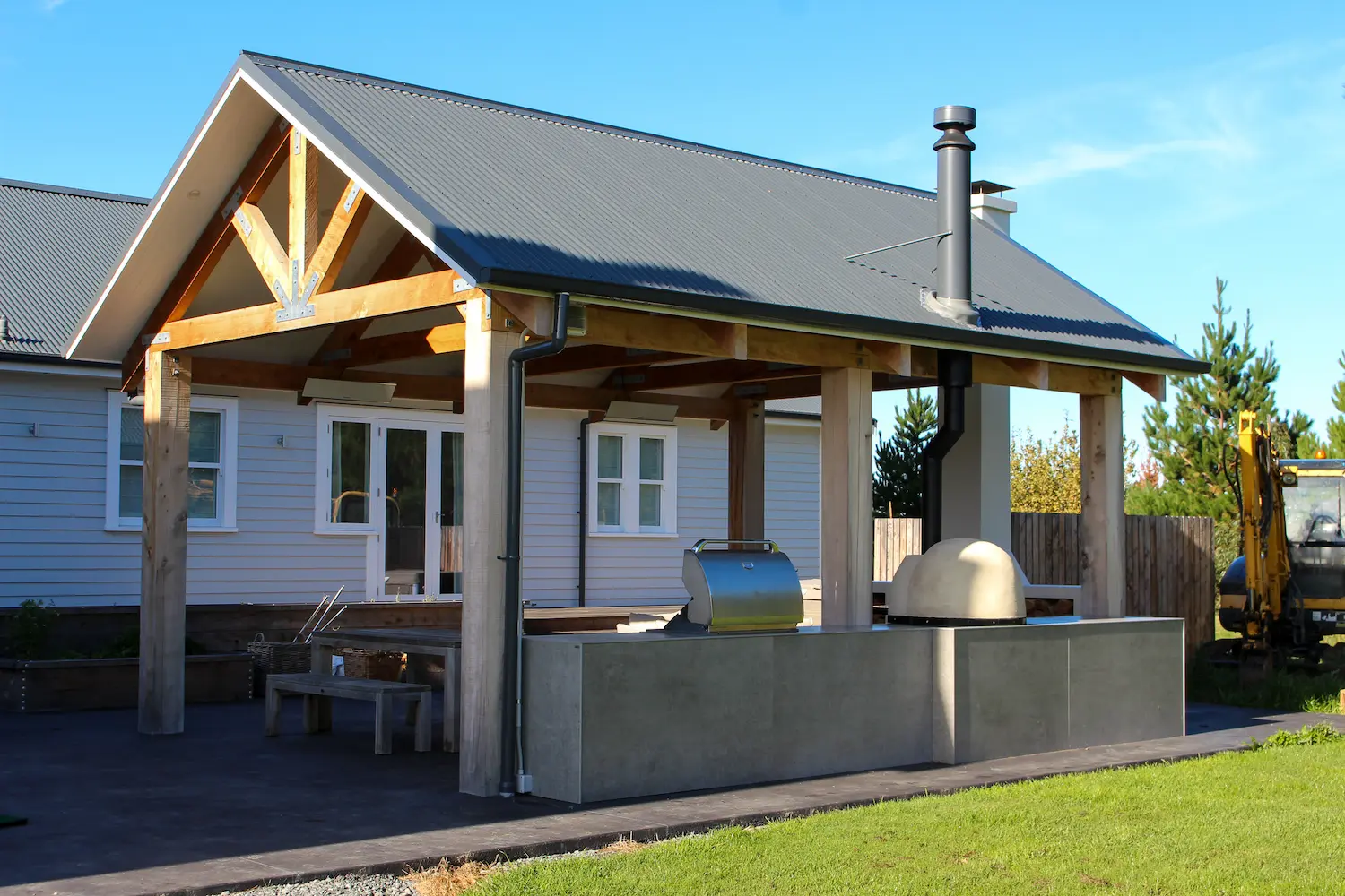 Outdoor pizza oven on a concrete countertop with stacked firewood stored below.