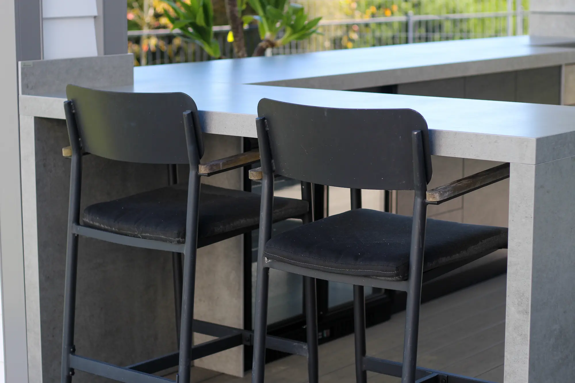 Two black bar stools with cushioned seats at a grey stone outdoor kitchen counter.