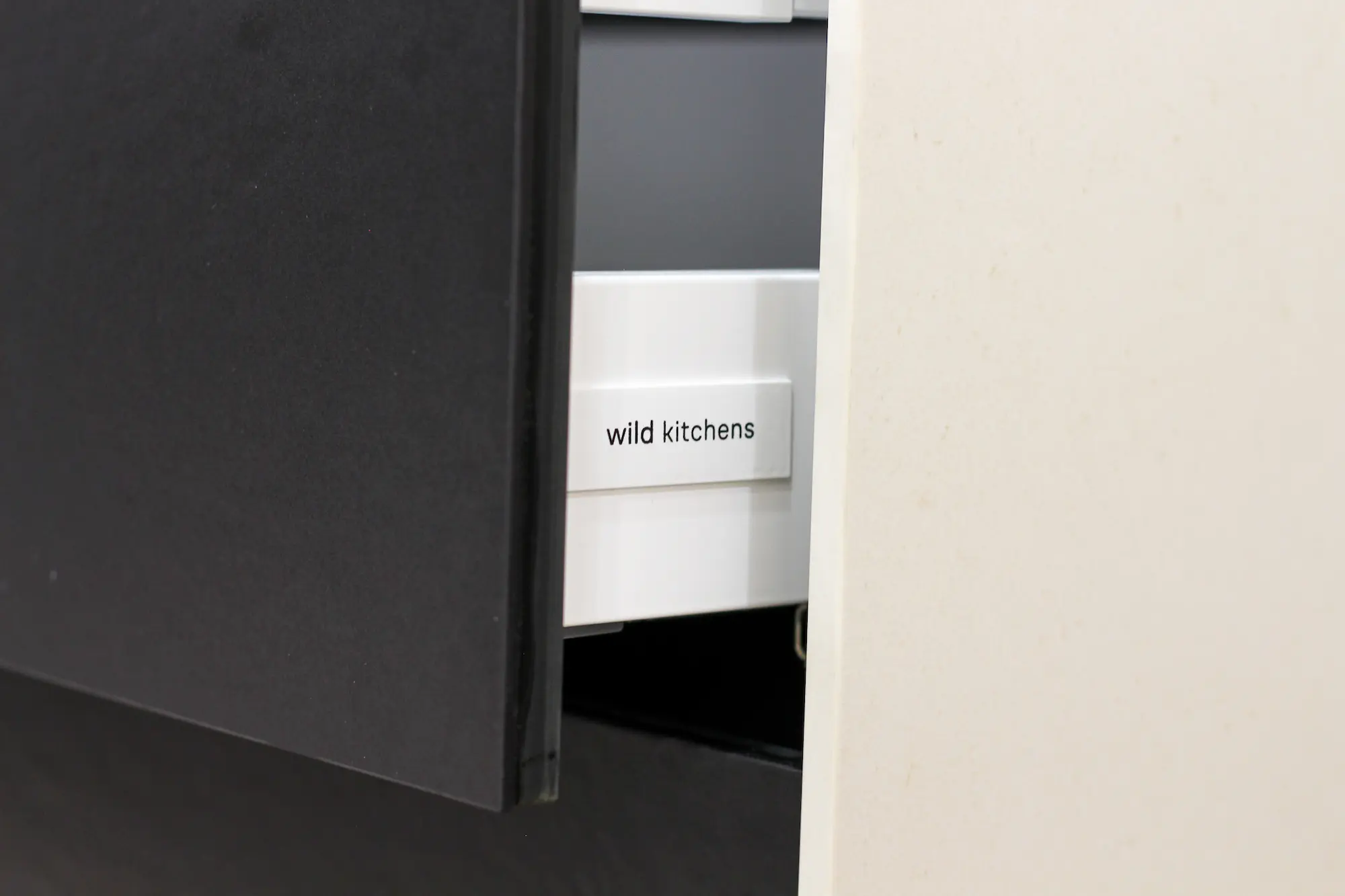 Partially open kitchen drawer with a white label that reads 'wild kitchens'.