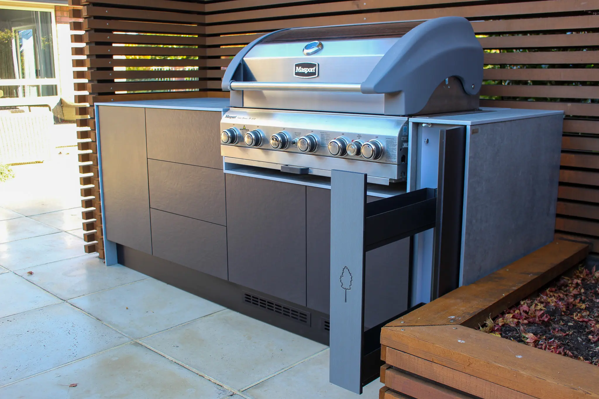 Outdoor pizza oven on a concrete countertop with stacked firewood stored below.