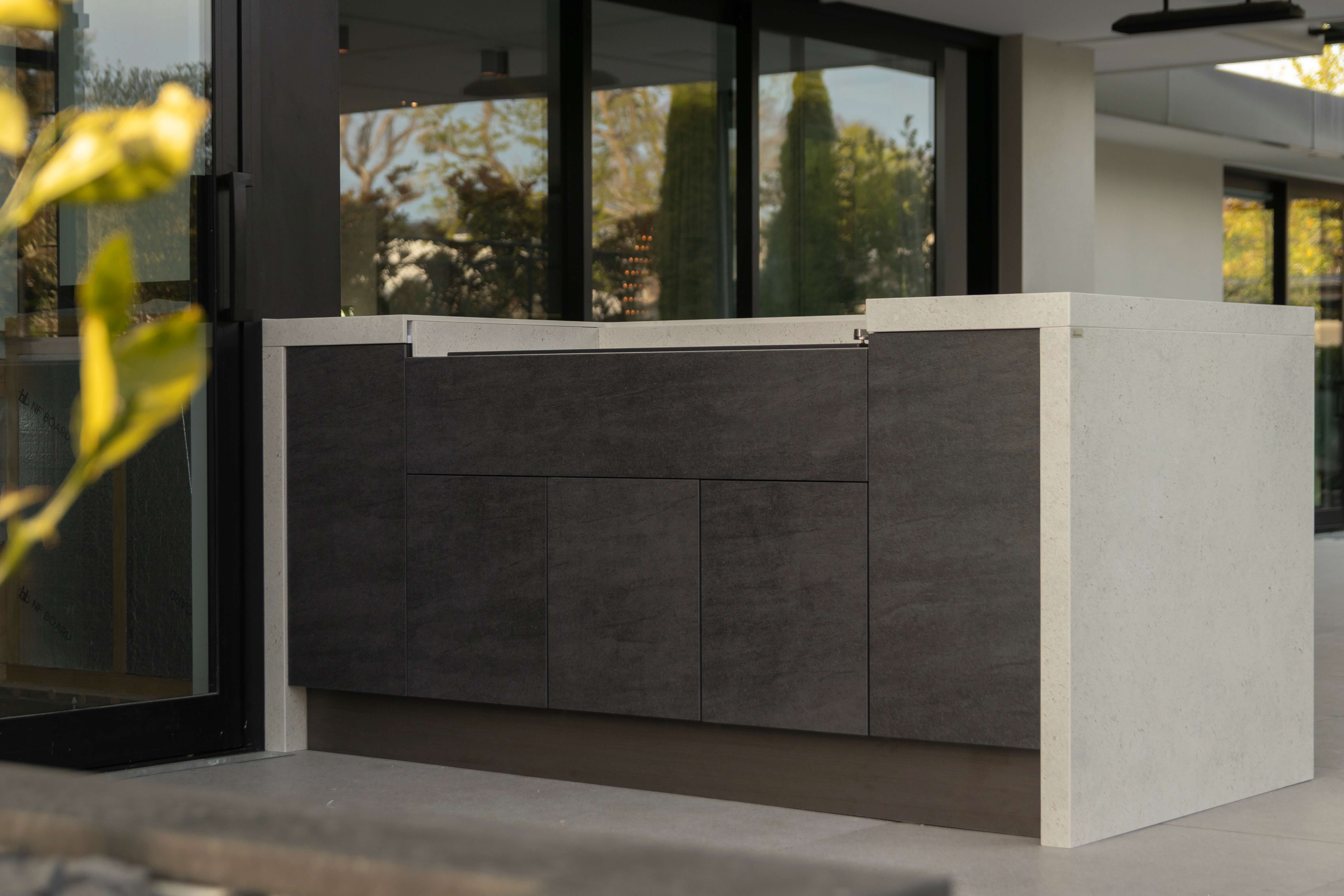 Modern outdoor kitchen unit with grey cabinets, open storage doors, a built-in grill, and a black mini fridge.
