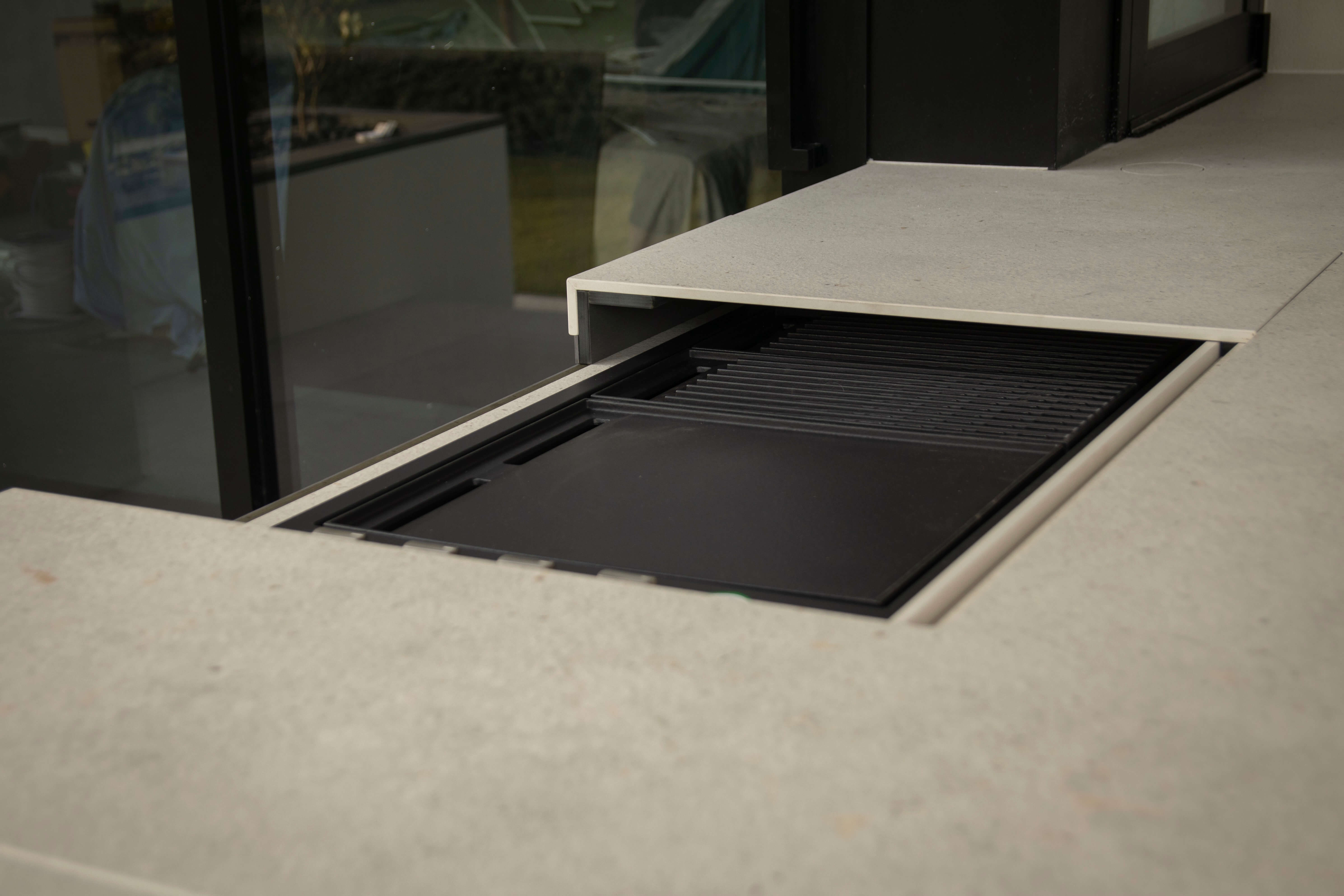Modern Dekton stone kitchen countertop with a stainless steel grill and stove knobs, alongside a black Artusi appliance.