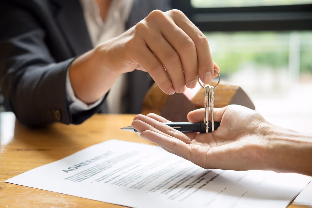 a professional woman handing over the keys to a house to someone else after they've signed official documents