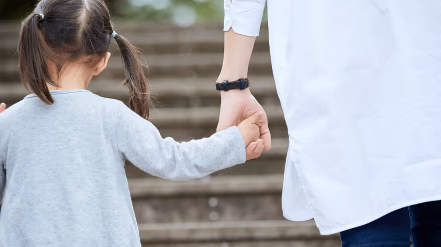 A parent and child hold hands while walking up a set of steps.