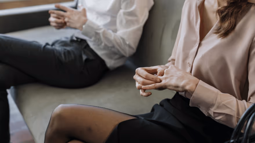 Two people sit apart on a couch, both removing wedding rings.