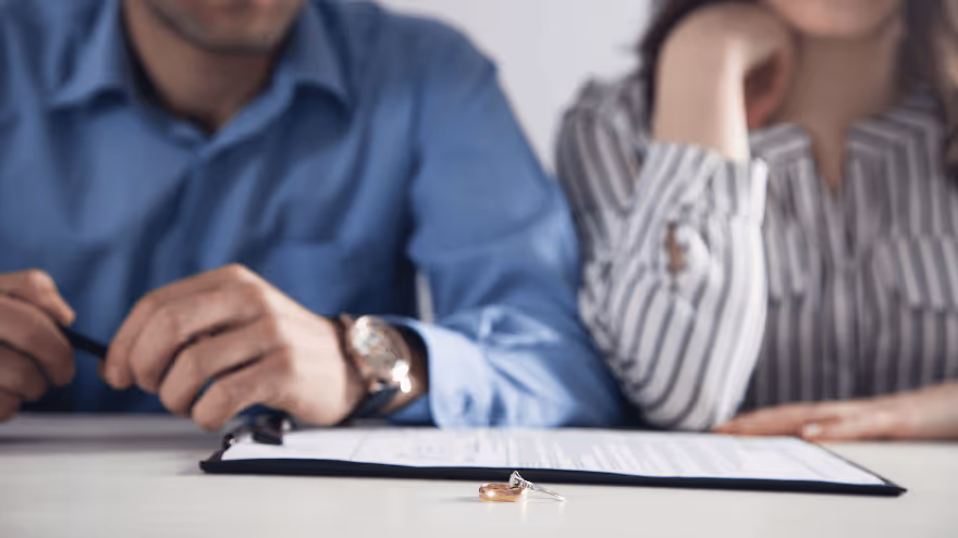 A couple sits at a table with divorce papers in front of them, their wedding rings placed on top of the document.