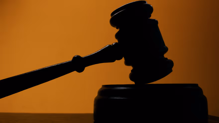 A judge’s gavel poised above a sound block against a warm orange background.