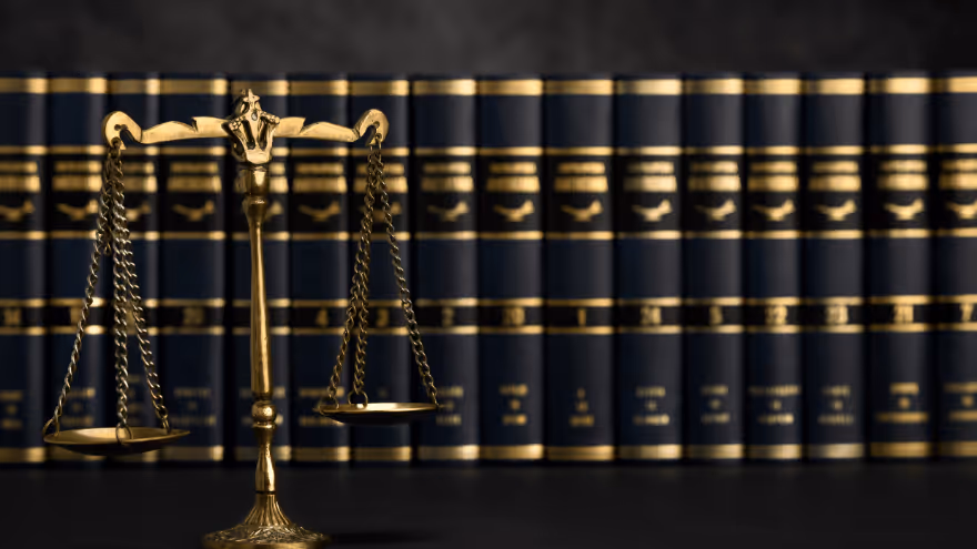 A bronze balance scale stands in front of a row of dark blue law books.
