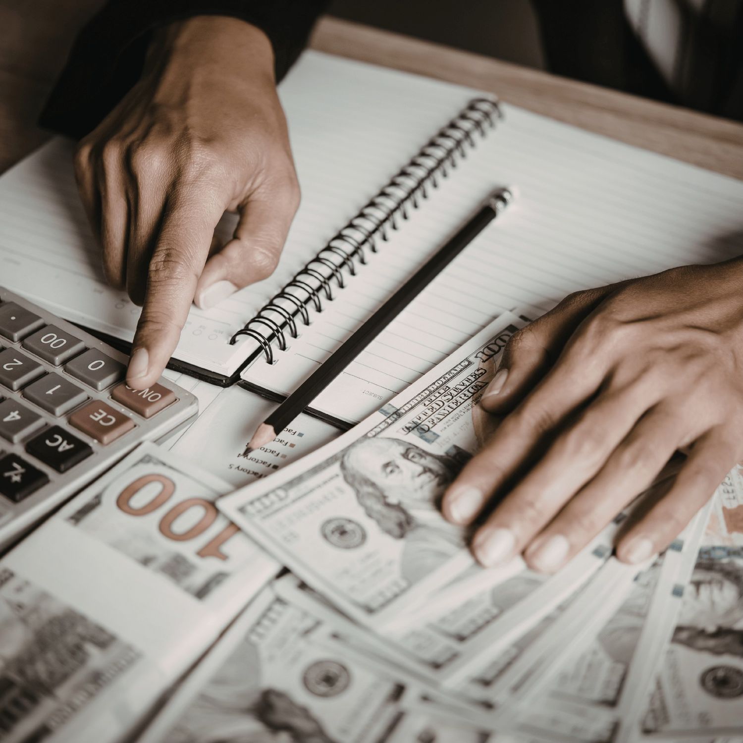 Person calculating finances with a calculator, notebook, and U.S. dollar bills spread on a desk.