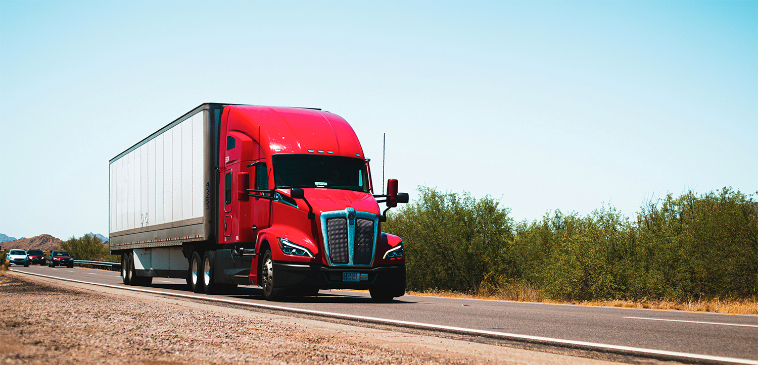Red semi-truck hauling a white trailer on a highway in North Texas under a clear sky, representing trucking companies that need bookkeeping support.