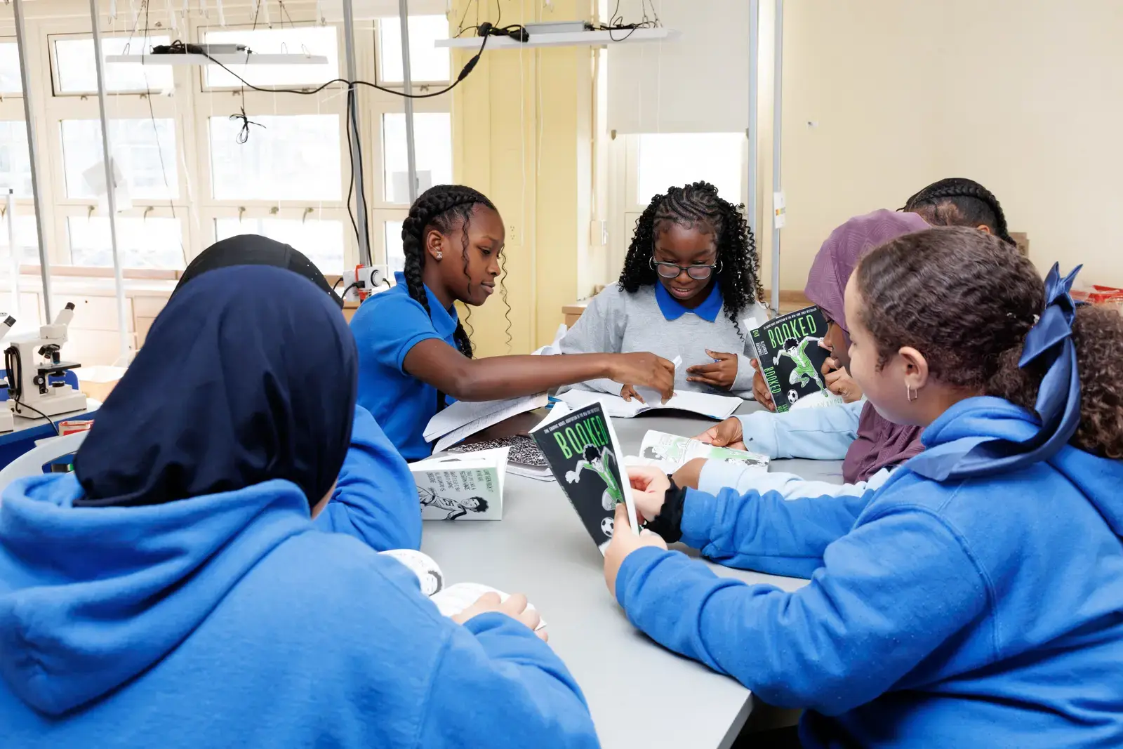 Students in school uniforms reading Booked together at a classroom table