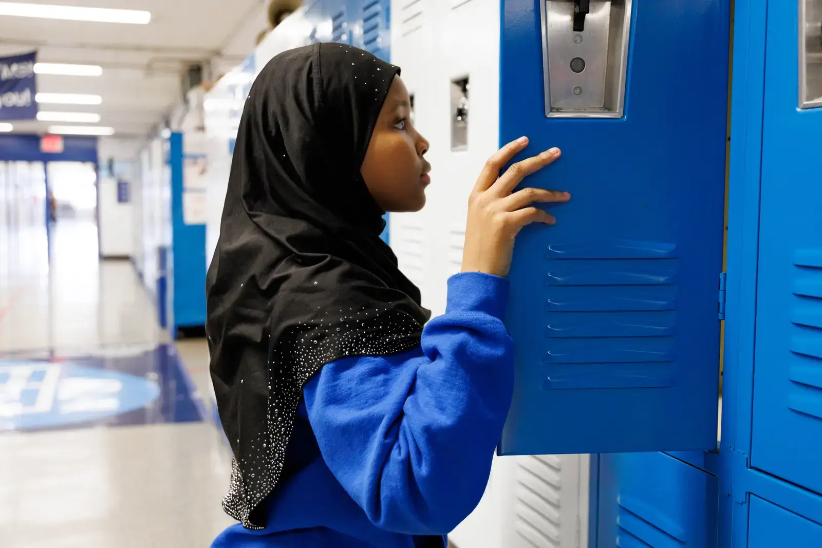 Student opening a blue locker in a school hallway