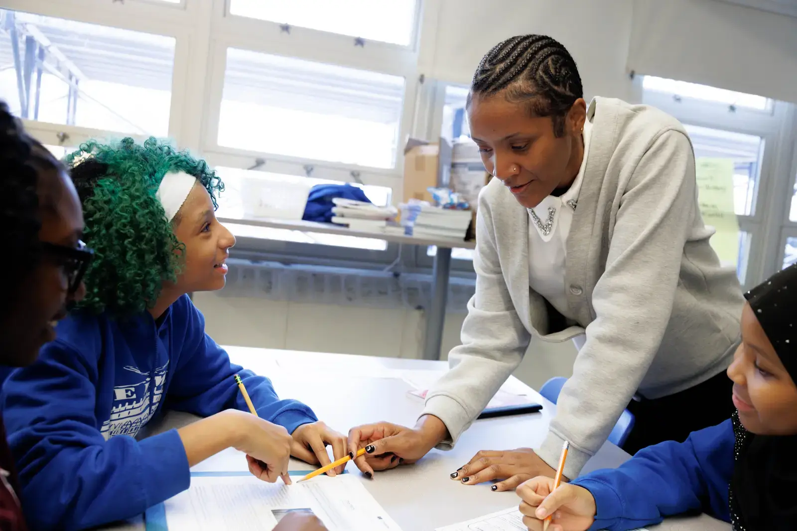 Teacher leaning over desk helping two students with classwork